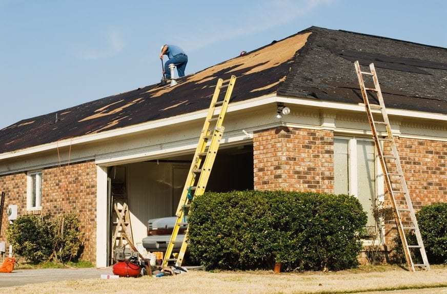 Roofer repairing the roof of a brick house in the suburbs.