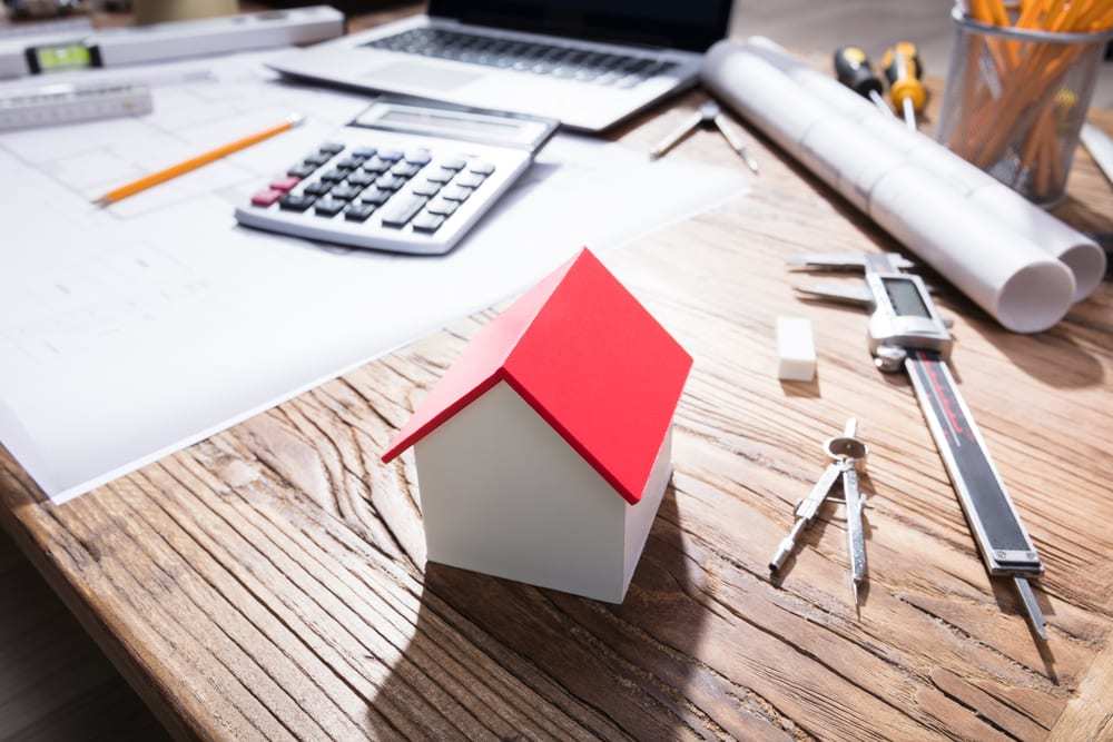 Close-up of house model on a wooden desk beside calculator and various tools