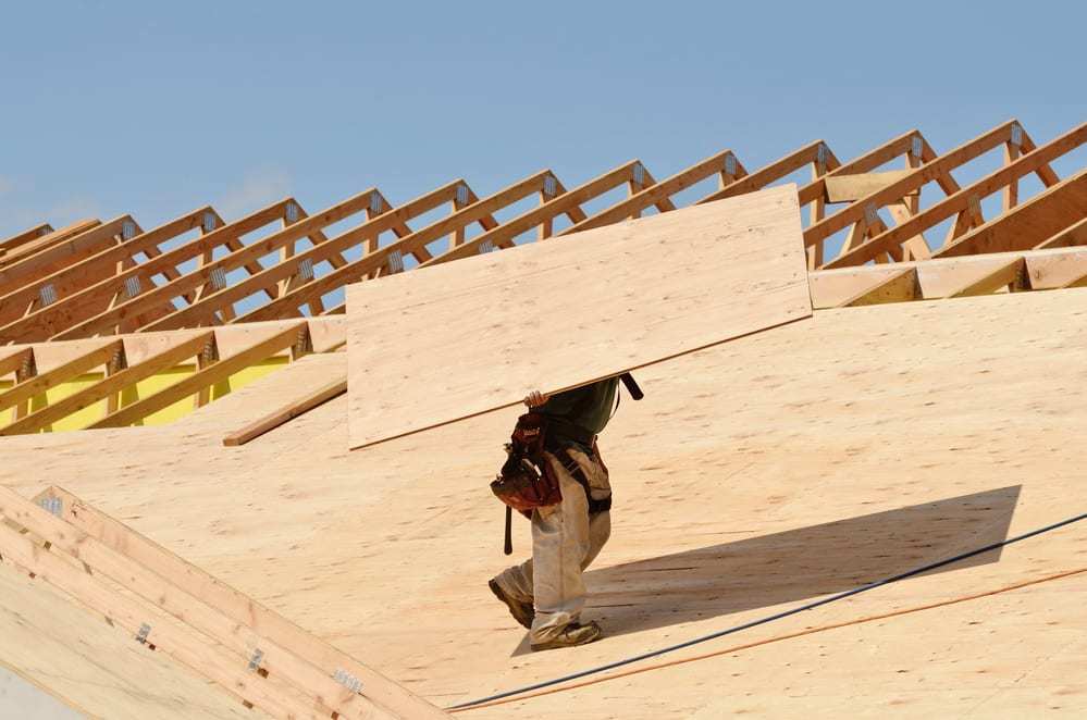 Roof specialist carrying a piece of plywood roof decking on roof in construction