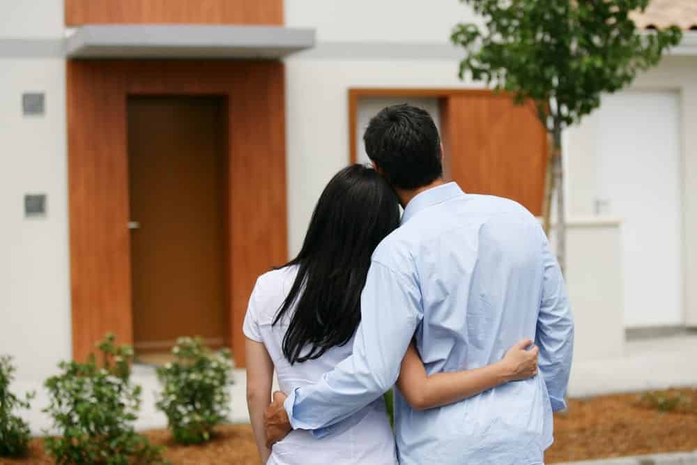 Young couple with arms around one another looking at home