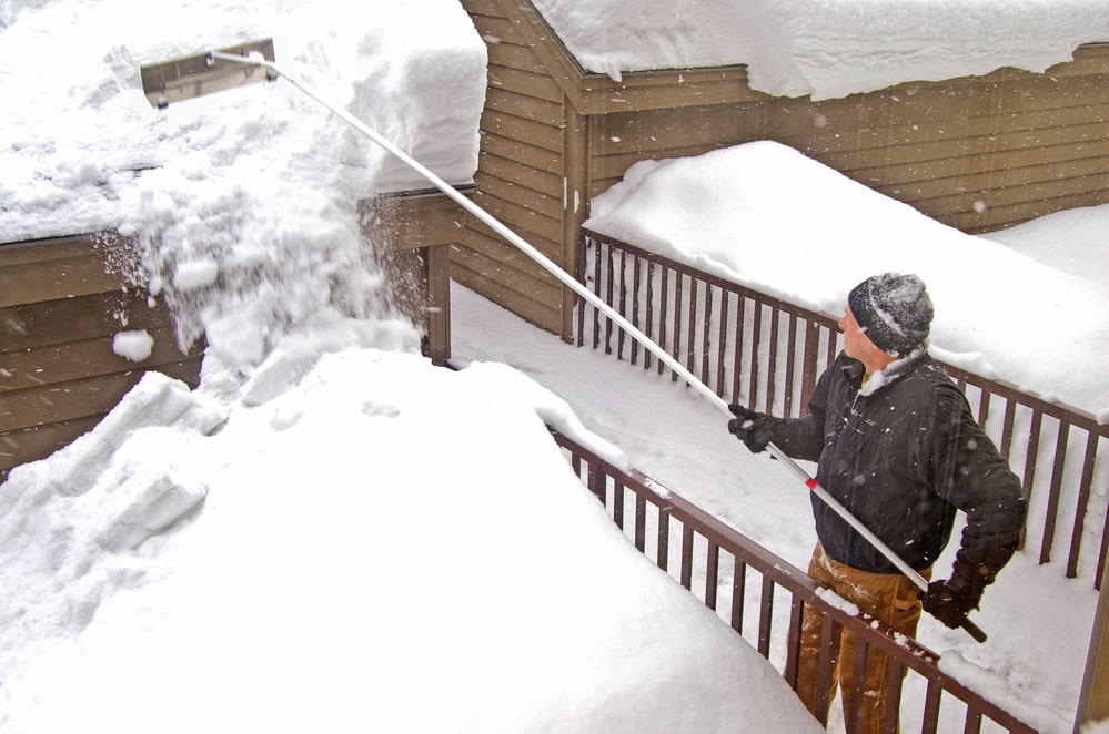 Man using tool to remove snow from roof