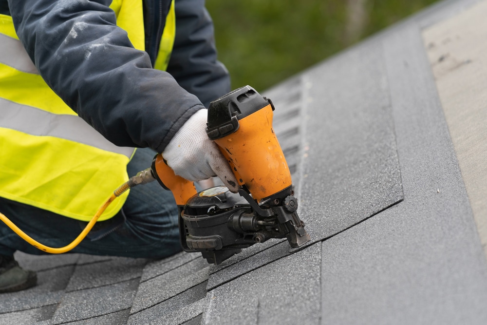 Roofer using nail gun to attach shingles to home roof