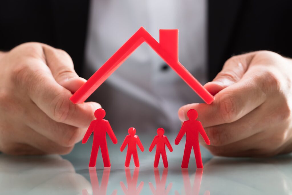 Business person hands holding red roof model over family of red figures