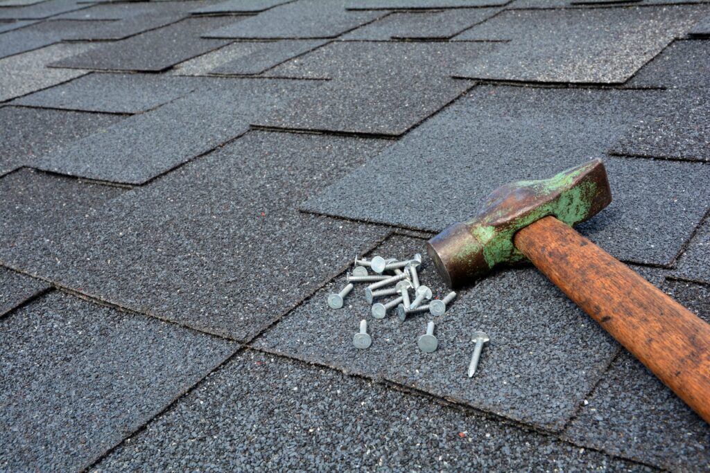 Close-up of hammer and nails resting on roof shingles