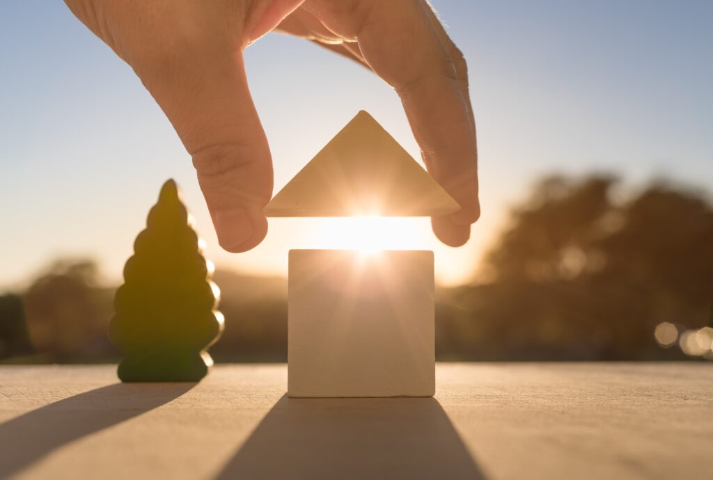 Hand holding roof over toy house, light shining through