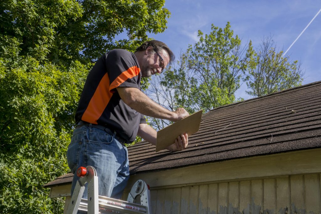 Roofer standing on ladder holding clipboard, making notes